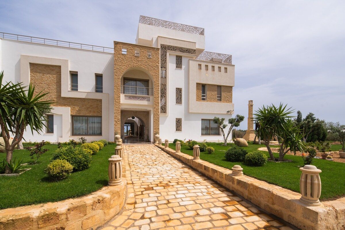 Façade de la villa Dar Aïcha à Tazarka, architecture blanche tunisoise avec pierre locale et jardin méditerranéen