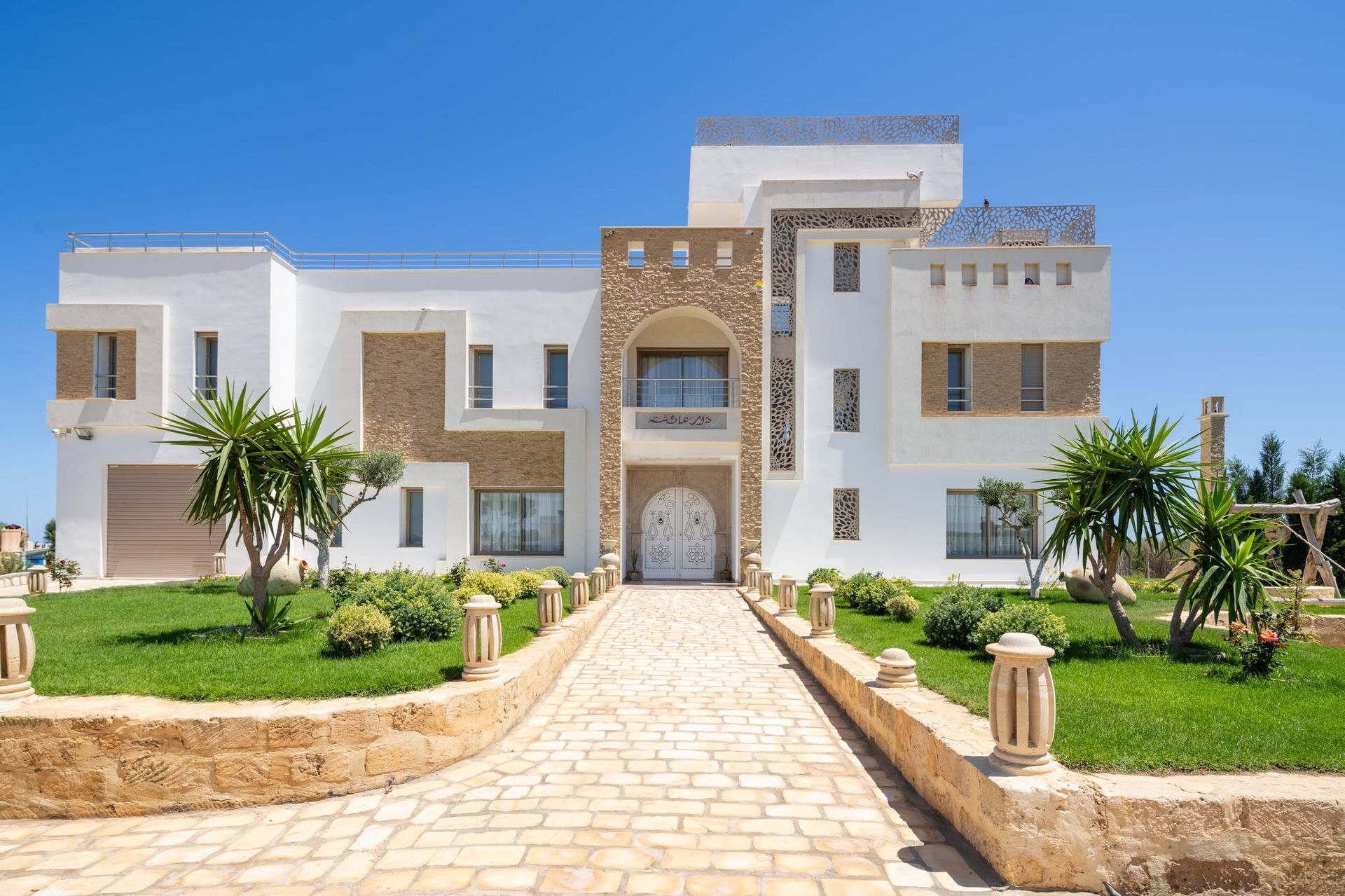 Vue large de la façade de la villa entourée de palmiers